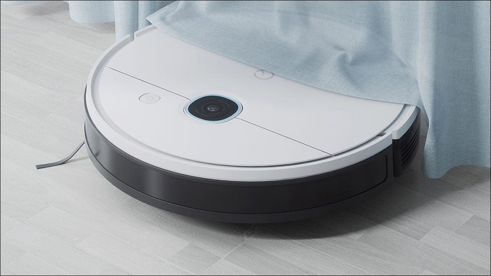 A robot vacuum rolling under curtains.