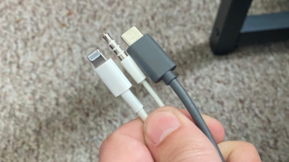 A man holding three cables: Lightning, AUX, and USB-C 